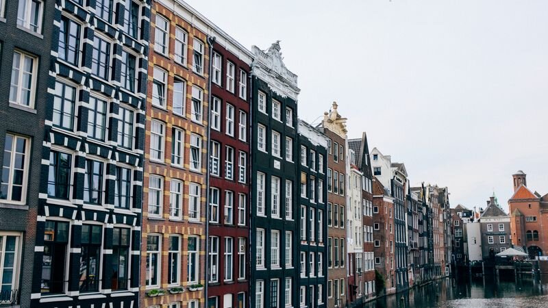 A row of narrow, colorfully gabled Amsterdam canal houses along the water