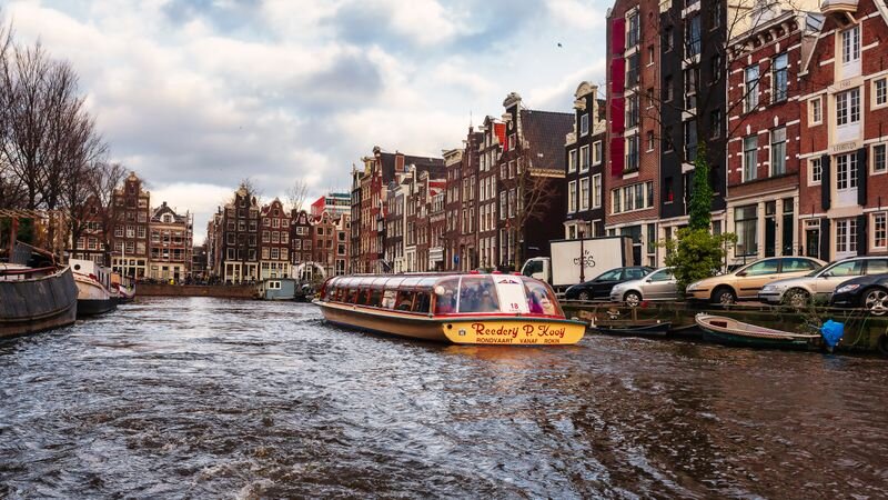 A canal cruise boat navigating an Amsterdam canal lined with narrow canal houses
