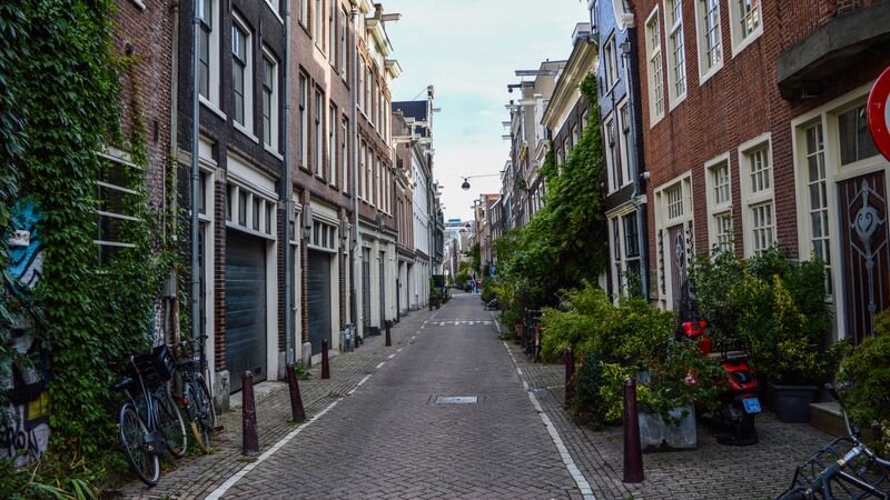 A narrow, quiet alley in Amsterdam lined with brick buildings, garage doors, and parked bicycles