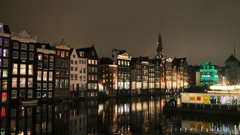 Amsterdam canal houses lit up at night, their windows glowing and reflecting on the water below