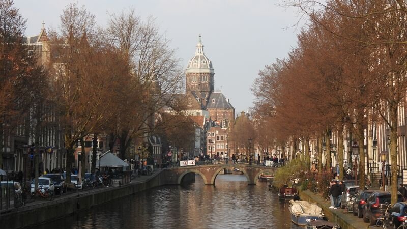 A canal lined with bare autumn trees, leading toward a domed church tower in the distance